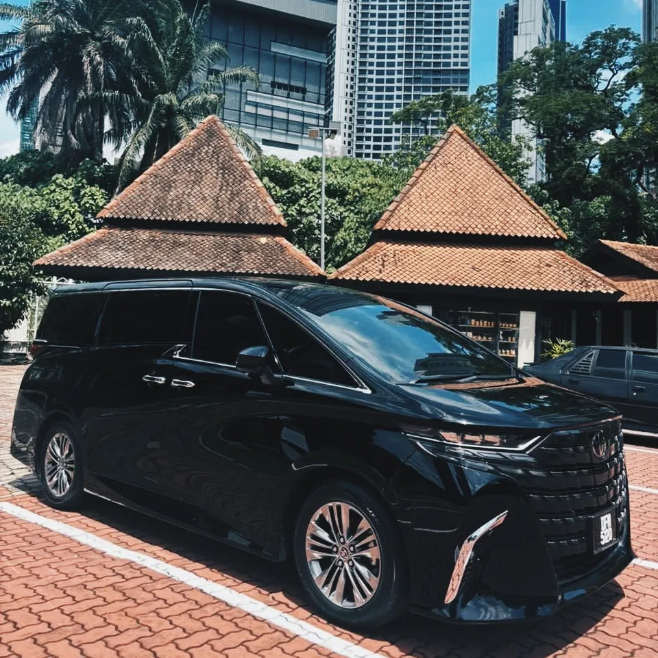 Black Toyota Alphard parked outside, Kuala Lumpur towers and tiled pavilion roofs behind